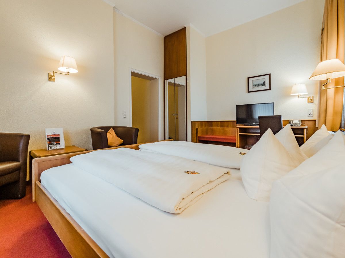 Habitación de hotel con una cama grande, un escritorio con silla, un televisor y una lámpara de escritorio.