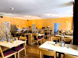 A restaurant with multiple tables and chairs, a kitchen area, and a door. - Hotel Am Marschiertor (Aachen)