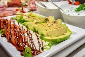 A white rectangular plate with sliced avocado, a grilled chicken breast, and a drizzle of sauce. - Hotel Am Marschiertor (Aachen)
