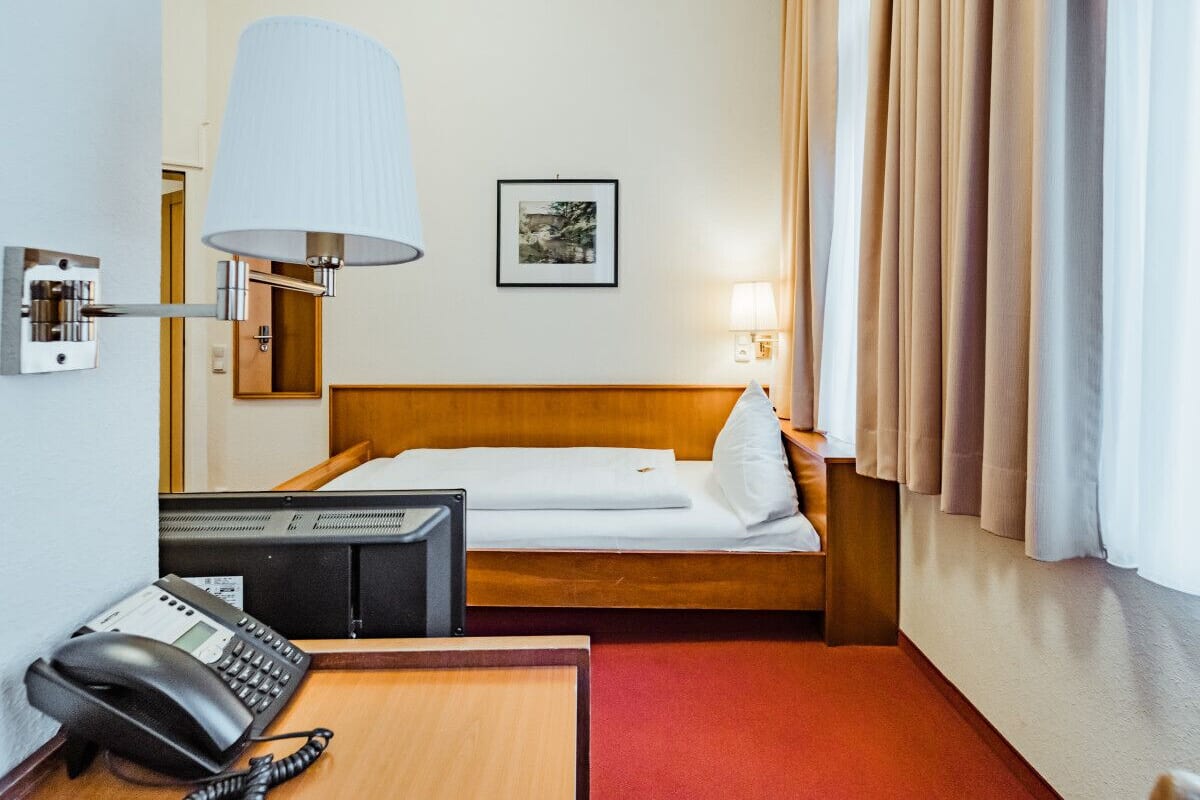 A hotel room with a bed, a desk with a telephone, a lamp, and a picture on the wall.