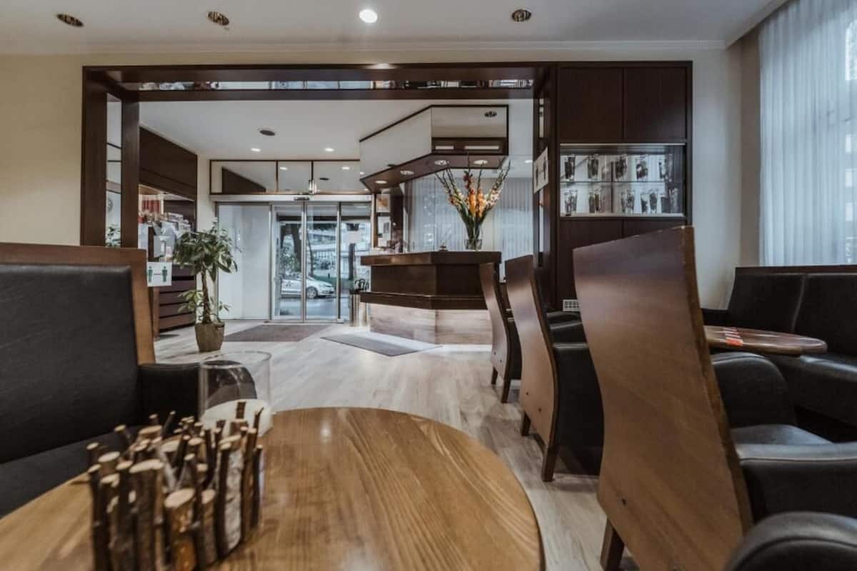 A modern hotel lobby with a reception desk, seating area, and a view of the street.