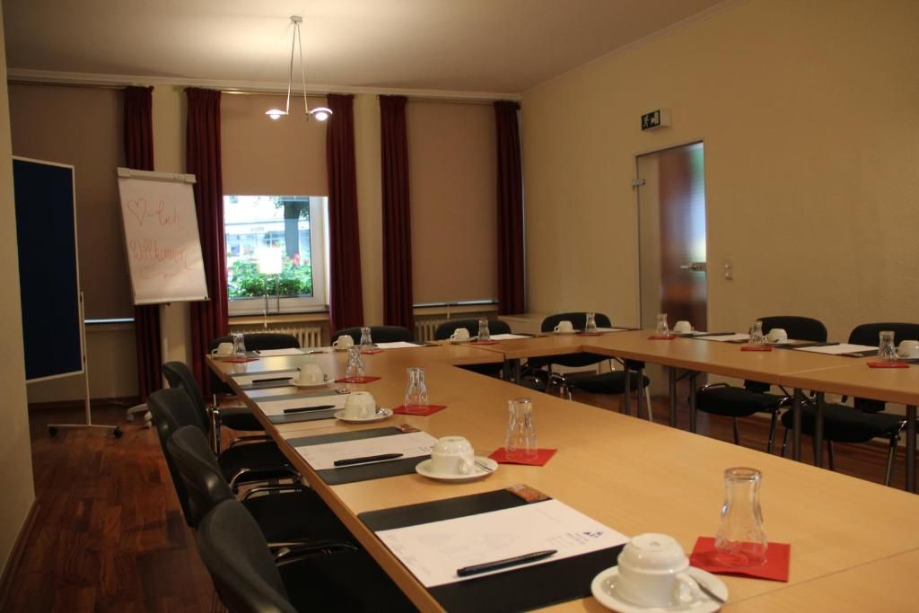 A conference room with a long table, chairs, a whiteboard, and a window with curtains.