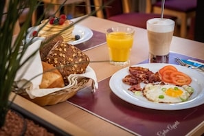 A breakfast setting with bread, eggs, bacon, tomatoes, and juice. - Hotel Am Marschiertor (Aachen)
