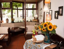 Un acogedor interior de restaurante con una zona de asientos tipo cabina, una mesa con un jarrón de girasoles y una máquina de coser antigua.
