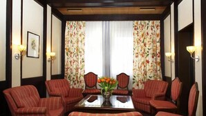 A room with a central table, four striped armchairs, floral curtains, and wall sconces. - Sternsoller (Ismaning)