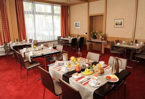 A hotel dining area with multiple tables set for breakfast, featuring a variety of dishes and beverages. - Sternsoller (Ismaning)