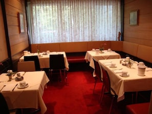 A dining area with tables set for service, a red carpet, and a window with floral curtains. - Sternsoller (Ismaning)