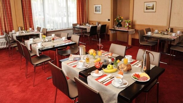 A hotel dining area with multiple tables set for breakfast, featuring a variety of dishes and beverages. - Sternsoller (Ismaning)