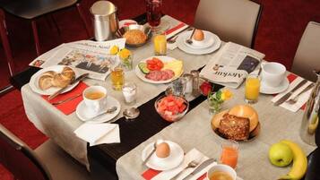 A breakfast table set with plates of eggs, toast, fruit, and beverages, along with a newspaper.