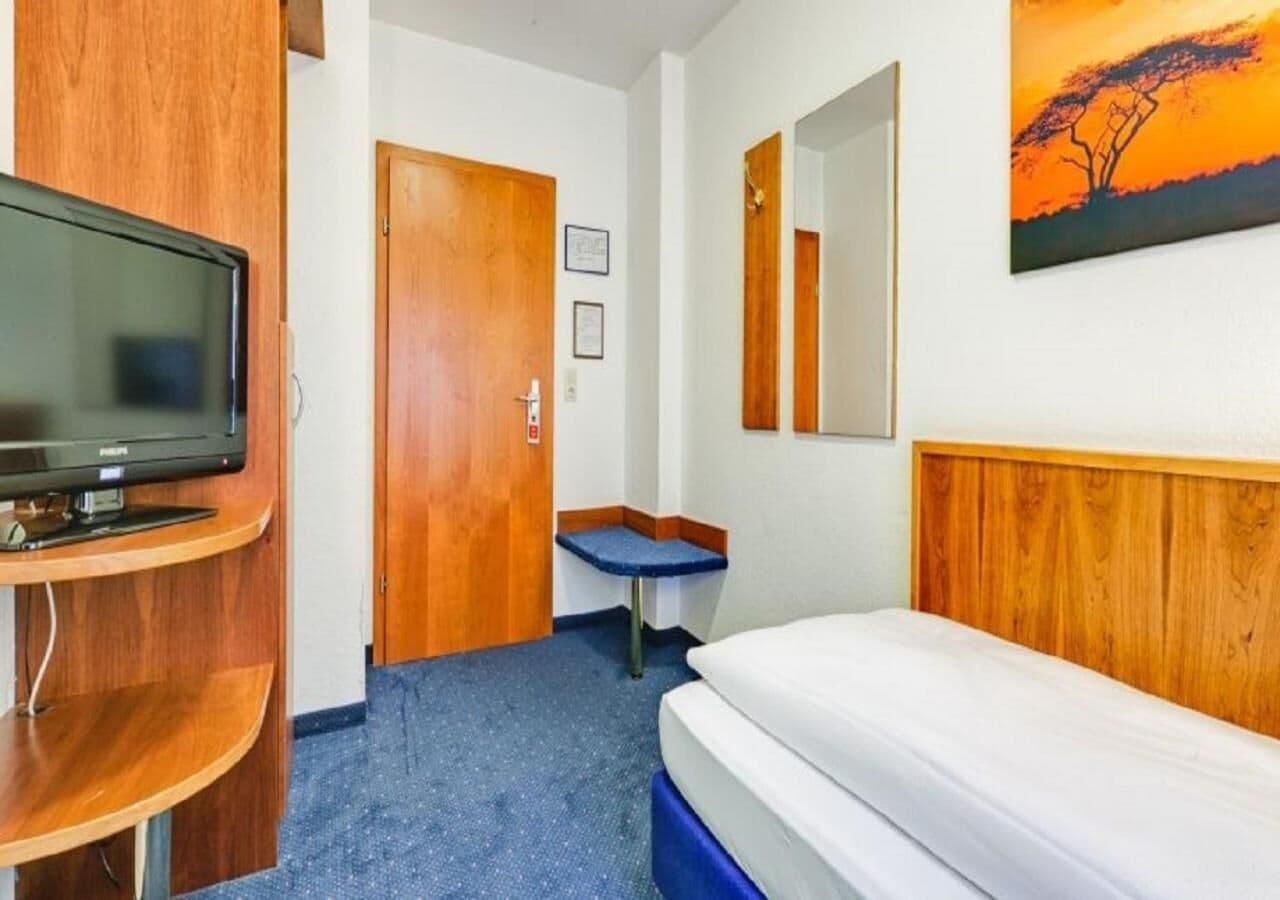 A hotel room with a bed, a television, a small table, and a painting on the wall.