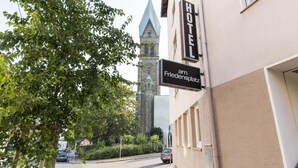 Hotellin kyltti, jossa lukee ”HOTEL am Friedensplatz”, ja taustalla näkyy kirkon torni.