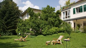 A grassy outdoor area with two wooden lounge chairs and a small table with a drink. - Villa Arborea (Augsburg)