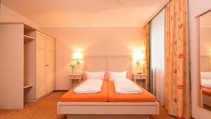 A double bed with white linens, two bedside tables with lamps, a wardrobe, and a mirror on the wall. - Villa Arborea (Augsburg)