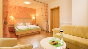 A hotel room with a bed, a sofa, a round table with fruit and a bottle, and a door. - Villa Arborea (Augsburg)