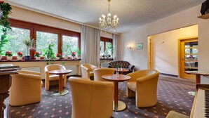 A hotel room with a large window, a chandelier, and several chairs and tables.