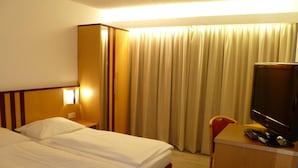 A hotel room with a bed, a desk with a television, and a window with curtains.