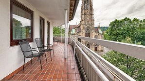 A balcony with two chairs, a tiled floor, and a view of a historic church.