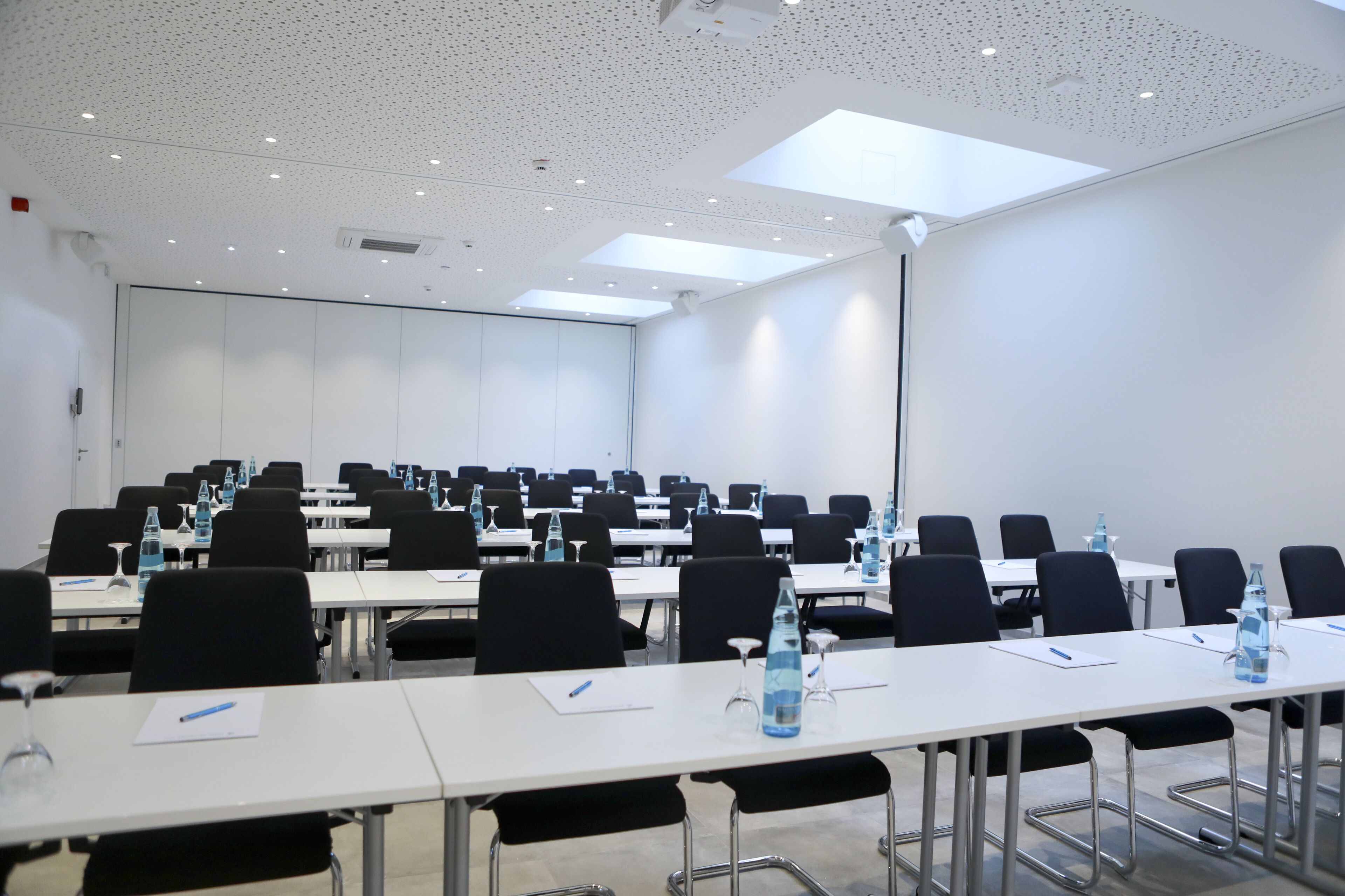 Un salón de conferencias con varias mesas, sillas y botellas de agua.