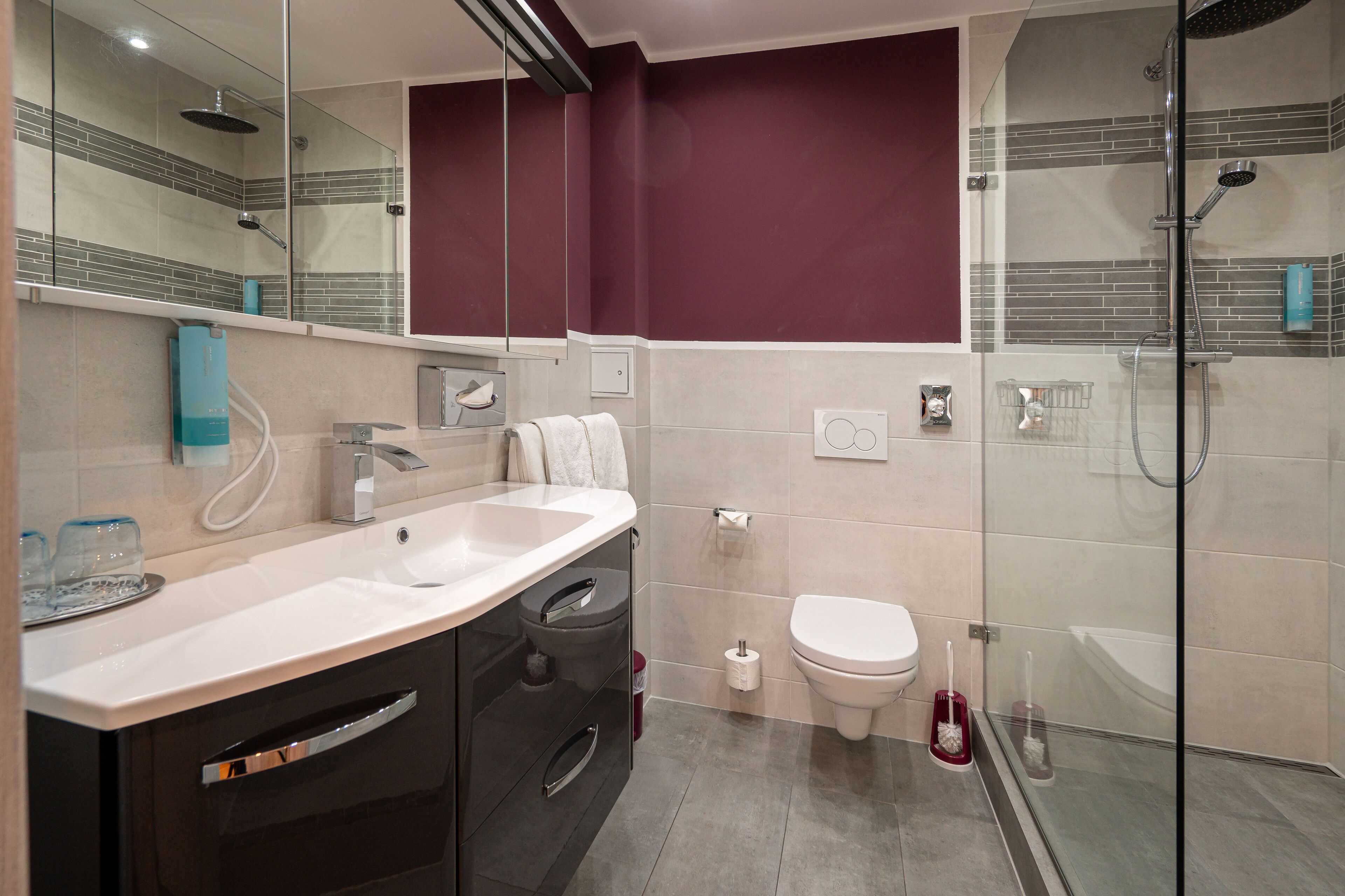 Een moderne badkamer met een douchecabine van glas, een witte wastafel en een donkere badkamerkast.