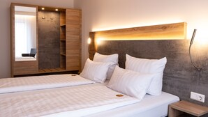 A double bed with white linens, a wooden wardrobe with a mirror, and a bedside table with a lamp. - Deutscher Hof (Kassel)