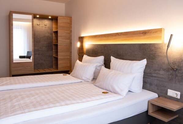 A double bed with white linens, a wooden wardrobe with a mirror, and a bedside table with a lamp. - Deutscher Hof (Kassel)