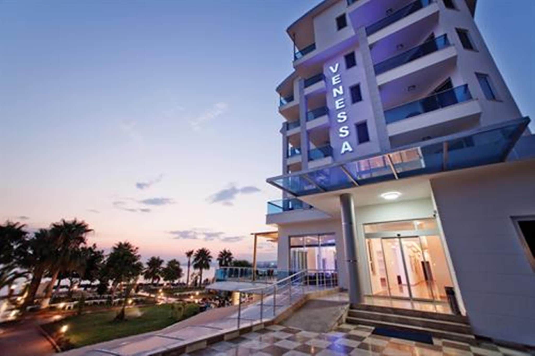 A multi-story hotel with a prominent 'VENESSA' sign, a glass balcony, and a well-lit entrance.