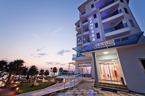 A multi-story hotel with a prominent 'VENESSA' sign, a glass balcony, and a well-lit entrance.