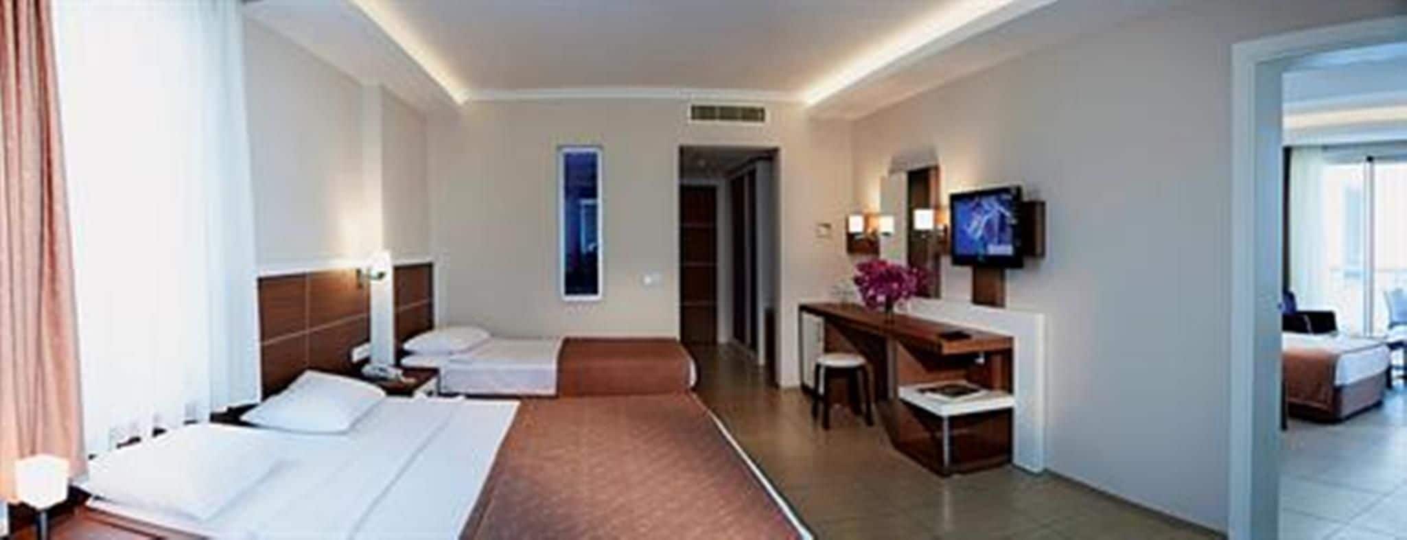 A hotel room with two beds, a desk, a TV, and a bathroom.