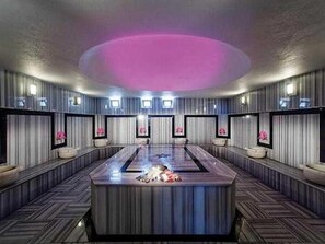 A modern hotel lobby with a central reception desk, seating areas, and a unique ceiling design.