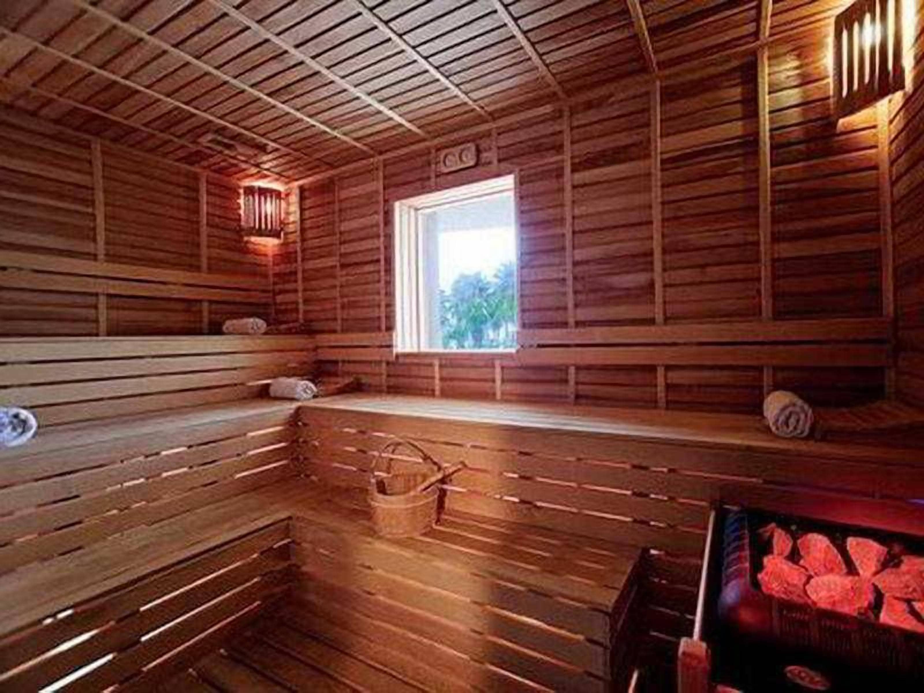 A sauna room with wooden benches, a window, and a heater.