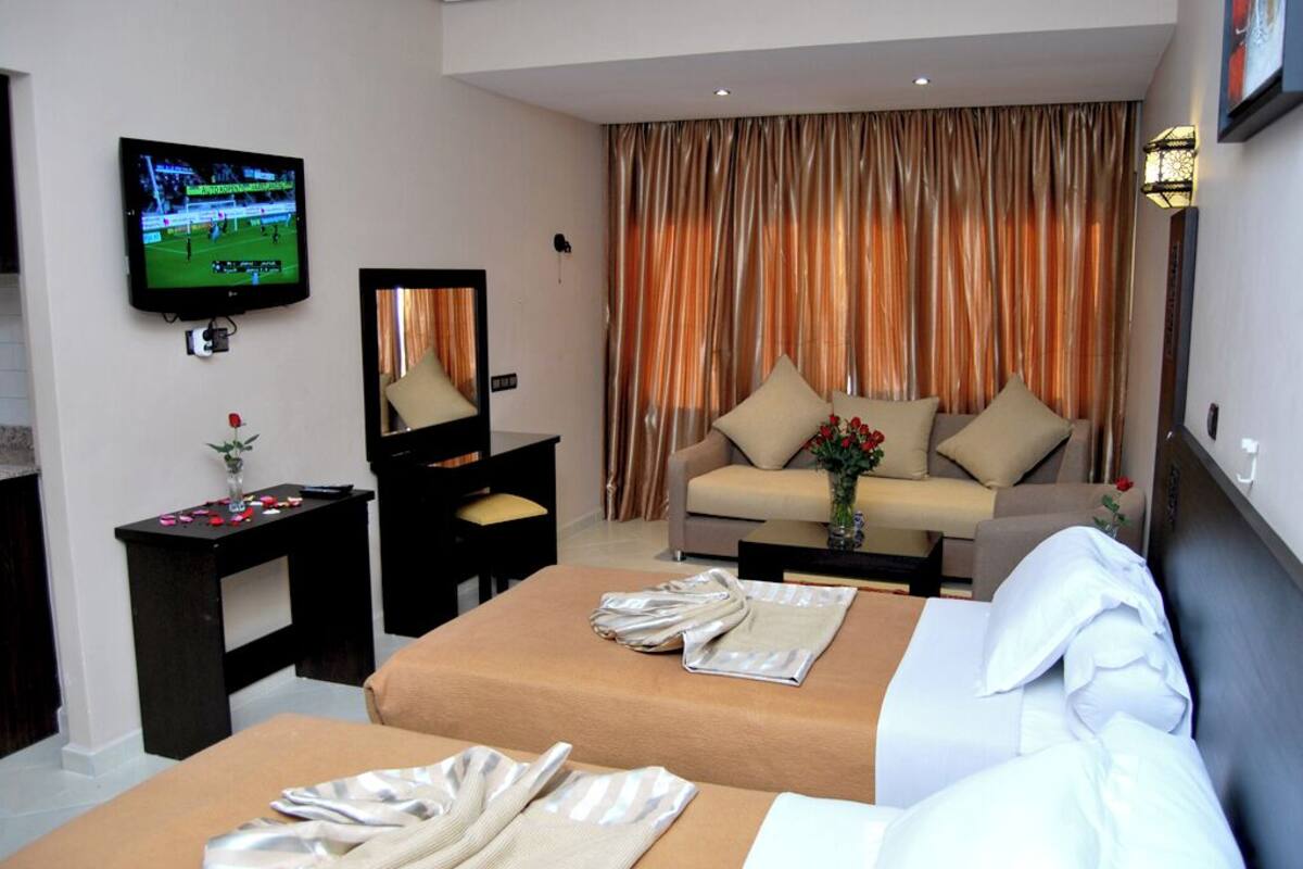A hotel room with two beds, a TV, a desk, a sofa, and curtains.