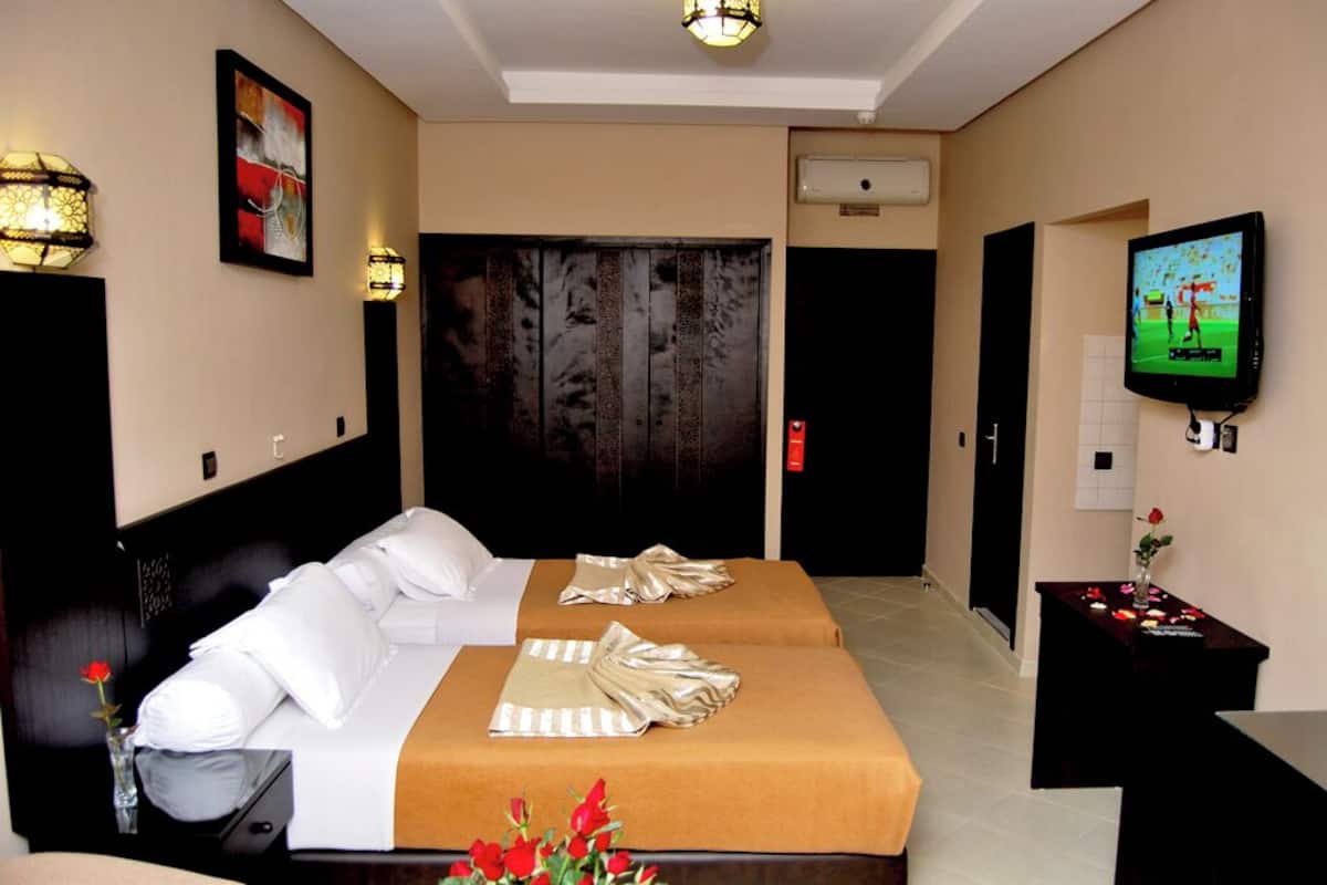 A hotel room with two beds, a TV, a desk, and a large wooden door.