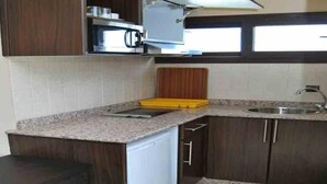 A kitchen with dark wooden cabinets, a granite countertop, a microwave, and a sink. - Suite Hotel Tilila (Agadir)
