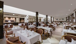 A spacious dining area with multiple tables set for guests, featuring a central column and a view of the kitchen area. - Sindbad Club (Hurghada)