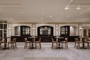 A bar area with multiple round tables and chairs, a central bar counter with a sign, and a patterned wall. - Sindbad Club (Hurghada)
