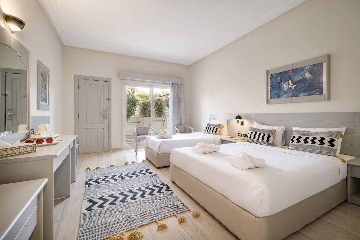 Habitació d'hotel amb dos llits, zona de seients, finestra gran i un quadre a la paret.