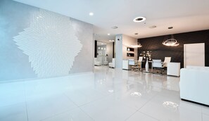 A modern hotel lobby with a large geometric wall design, a reception desk, seating area, and a dark brick accent wall. - Grifid Hotel Encanto Beach (Varna)
