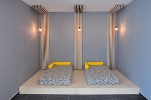 A room with two beds, each with a patterned mattress and yellow pillows, against a grey wall with vertical slats. - Grifid Hotel Encanto Beach (Varna)