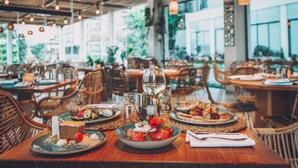 A restaurant with wooden tables, wicker chairs, and a view of greenery outside. - Grifid Hotel Encanto Beach (Varna)