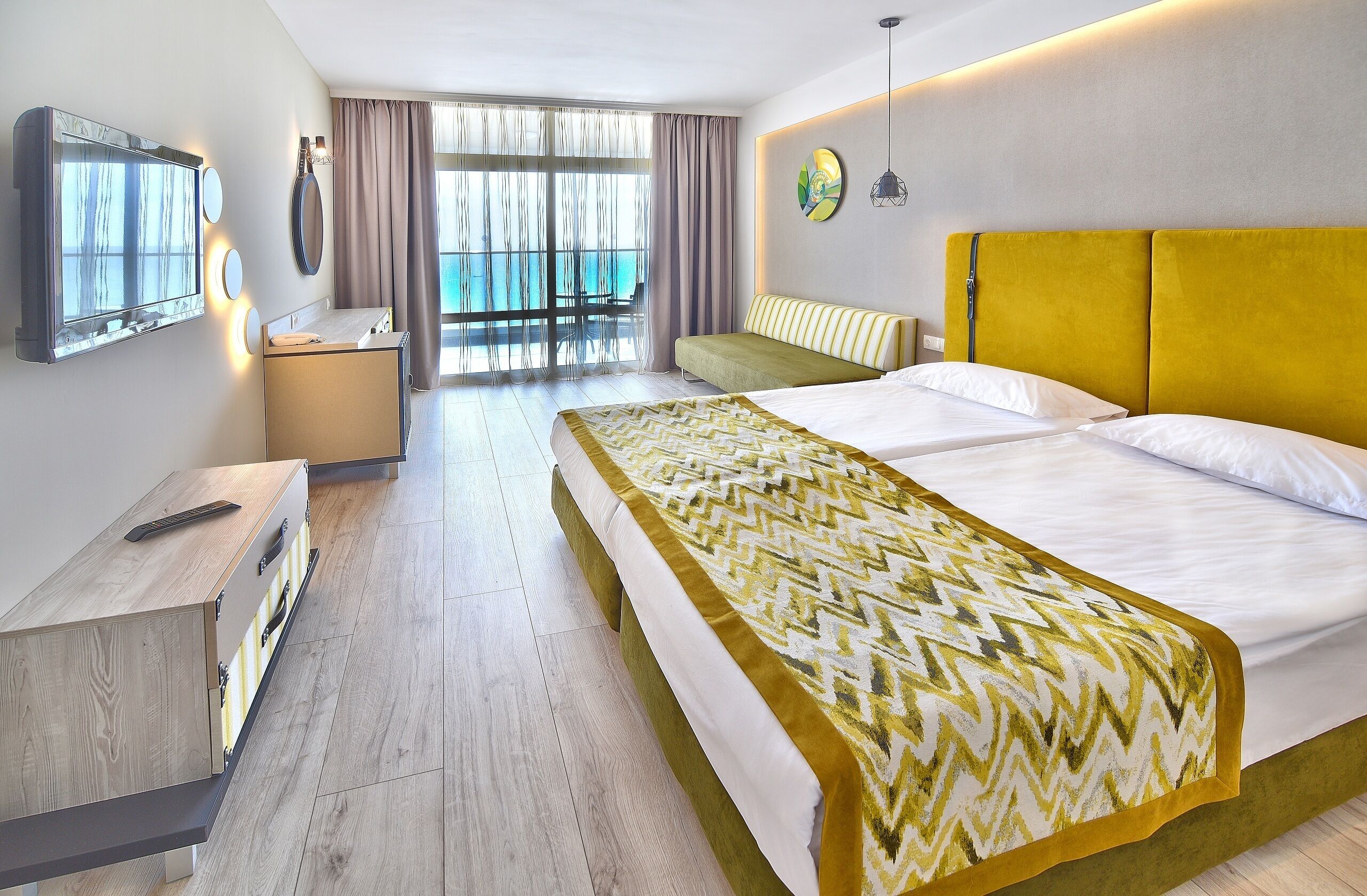 A hotel room with a bed, a desk, a chair, a large window with a view, and a balcony.