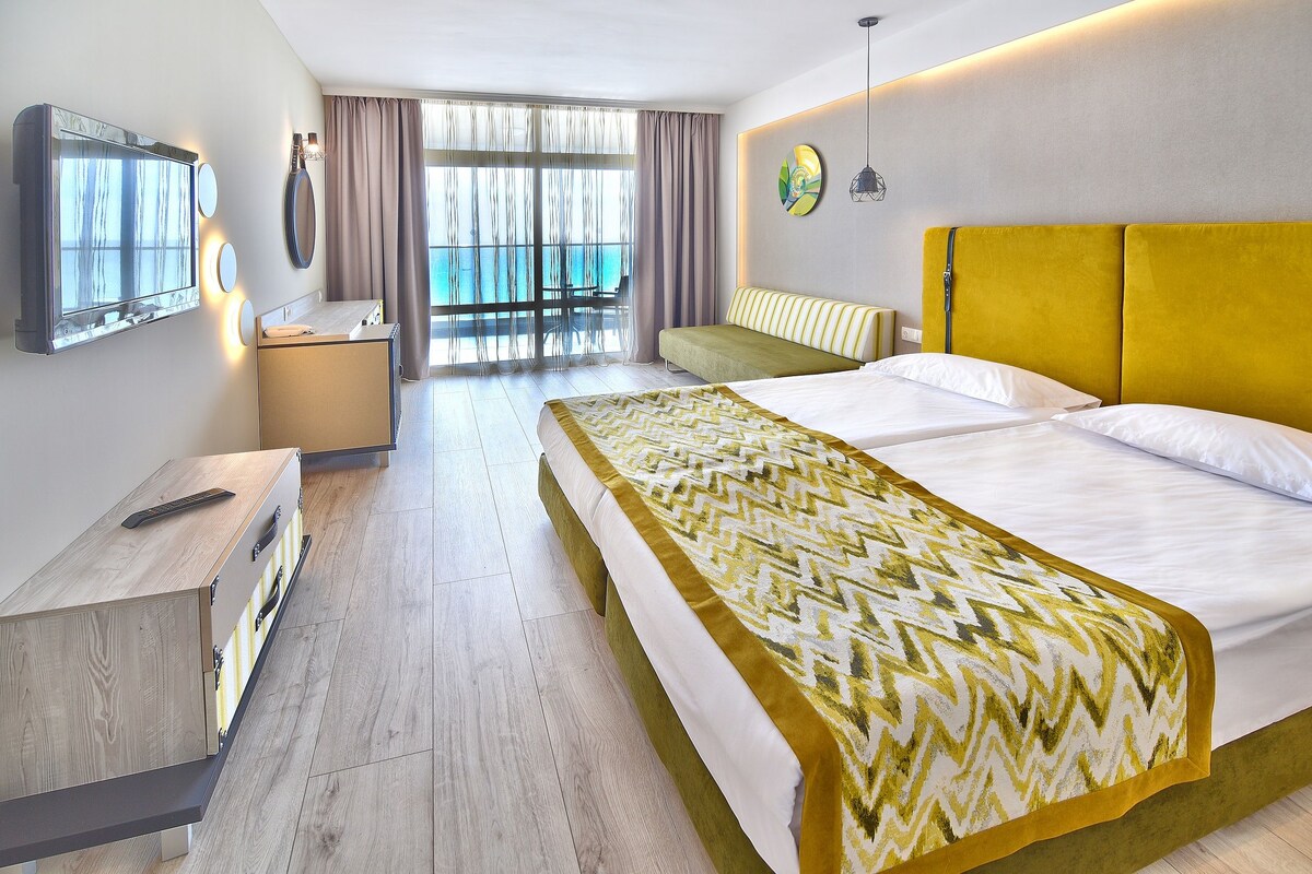 Habitación de hotel con cama, escritorio, silla, un ventanal con vistas y balcón.