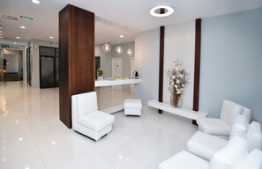 A modern reception area with white sofas, a wooden accent column, and a reception desk with a vase of flowers.