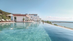A poolside area with lounge chairs and umbrellas, a building with a flat roof, and a view of the sea. - Grifid Hotel Encanto Beach (Varna)