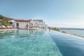 A poolside area with lounge chairs and umbrellas, a building with a flat roof, and a view of the sea. - Grifid Hotel Encanto Beach (Varna)