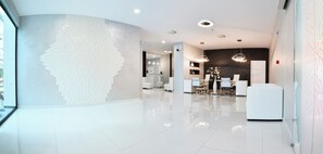 A modern hotel lobby with a curved wall, a reception desk, seating area, and a large decorative wall piece.