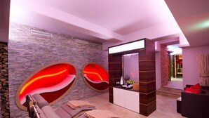 Ein moderner Wellnessraum mit Massagesesseln, einer Steinwand und einem Empfangstisch mit Spiegel.