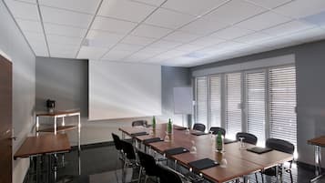 A conference room with a long table, chairs, a projector screen, and a window with blinds.
