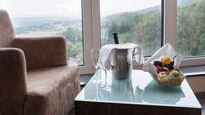 Ein Zimmer mit Blick auf einen Wald und Berge, eine Kaffeemaschine, ein Glas Wein und ein Obstkorb auf einem Tisch.