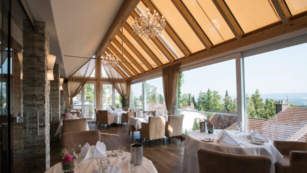 Ein Restaurant mit gedeckten Tischen, großen Fenstern und Blick auf die Landschaft.