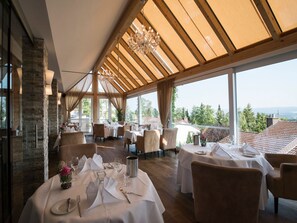 A restaurant with tables set for dining, large windows, and a view of the landscape.